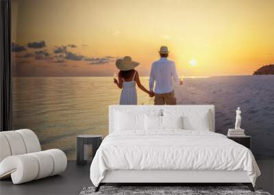 A beautiful couple stands on a tropical beach and watches the sunset with a drink in their hand Wall mural