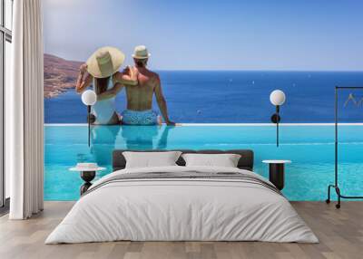 A couple hugging at the edge of an infinity pool and enjoying the view to the blue, mediterranean sea during summer vacation time Wall mural