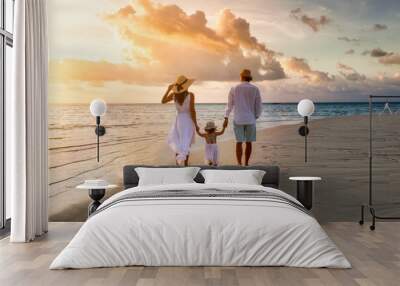 A elegant family in white summer clothing walks hand in hand down a tropical paradise beach during sunset tme and enjoys their vacation time Wall mural