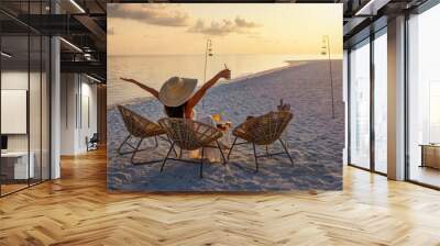 A elegant woman in a white dress enjoys the tropical sunset with a cocktail on a beach in the Maldives islands Wall mural