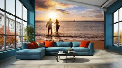 A happy holiday couple enjoys a tropical beach during golden sunset time and runs in the sea Wall mural