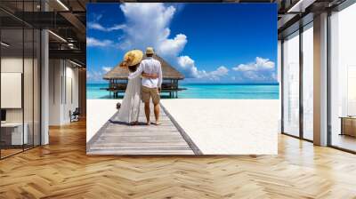 A happy holiday couple in summer clothing stands hugging on a tropical beach in the Maldives islands Wall mural