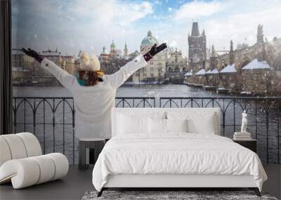 A happy tourist woman in winter clothing enjoys the view of the skyline of Prague with Charles Bridge and old town with snow  Wall mural