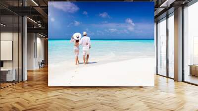 A hugging honeymoon couple walks down a tropical beach with turquoise sea and sunshine  Wall mural