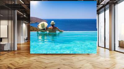 A loving couple with hats hugging at the edge of an infinity pool and enjoying the view to the blue, mediterranean sea during summer vacation time Wall mural