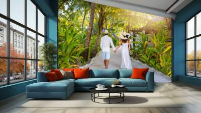 A luxury couple in white summer clothing walks on a tropical island with lush green and Palm Trees at the Maldives, Indian Ocean Wall mural