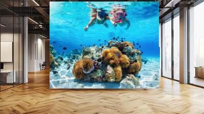 A mother and daughter snorkeling in tropical ocean over a colorful coral reef with fish during their summer vacations Wall mural