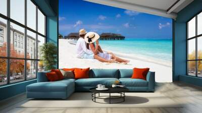 A romantic couple in white summer clothes sits hugging in the fine sand of a tropical beach in the Maldives Wall mural