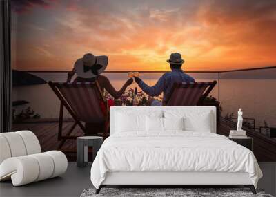 A romantic couple sitting in lounge chairs on summer vacation enjoys the sunset over the mediterranean sea with a glass of wine Wall mural