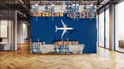 Aerial top view of a cargo plane flying above container freight port with docked ships and loading and unloading by cranes and trucks Wall mural