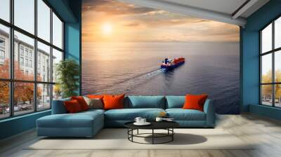 Aerial view of a container cargo ship sailing over calm sea into the sunset Wall mural