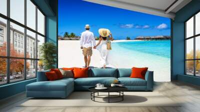 Happy couple in white summer clothing and with hats walks on a tropical paradise beach with turquoise sea in the Maldives islands Wall mural