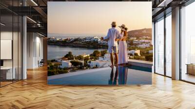 Happy couple on vacation time enjoys the summer sunset over the Aegean Sea by the swimming pool with an aperitif drink Wall mural