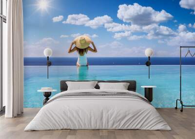 Summer holiday concept with a woman with sunhat sitting at the endge of a big infinity pool Wall mural