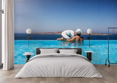 Traveler couple with sunhats hugging in a infinity pool and enjoying the view to the mediterranean sea Wall mural