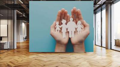 a pair of hands holding paper cutout people on blue background, family concept with copy space Wall mural