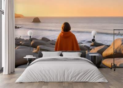 A person peacefully sits on a rock, gazing out at the vast ocean Wall mural