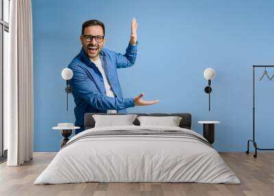 Cheerful businessman demonstrating something with copy space while standing on blue background Wall mural