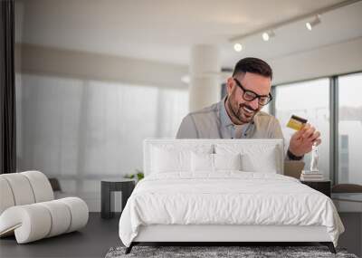 Cheerful entrepreneur making online payment while using laptop at office desk Wall mural