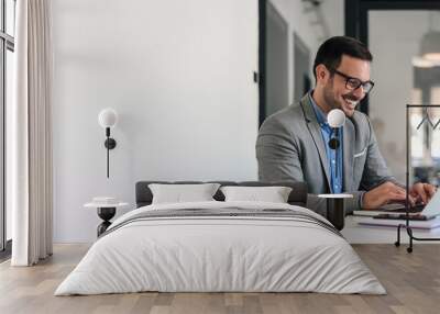 Cheerful male businessman entrepreneur professional working on laptop while sitting at office desk Wall mural