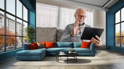 cheerful senior man having video call on tablet sitting on the couch at home elderly man wearing eye Wall mural