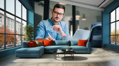 Close up portrait of handsome man working from home office taking reading and writing notes in note pad while working on laptop computer casual businessman entrepreneur focused doing research Wall mural