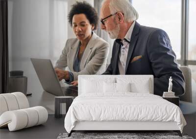 Confident business partners discussing while working on laptop during meeting. Wall mural