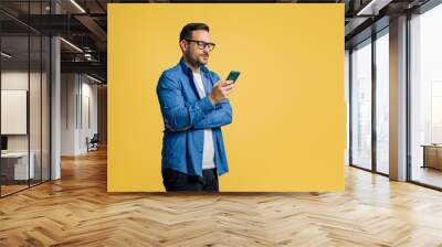 Confident handsome entrepreneur text messaging over mobile phone while standing on yellow background Wall mural