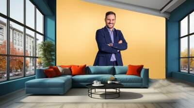 Confident handsome mid adult businessman wearing elegant blue suit with arms crossed smiling and posing on isolated orange background Wall mural