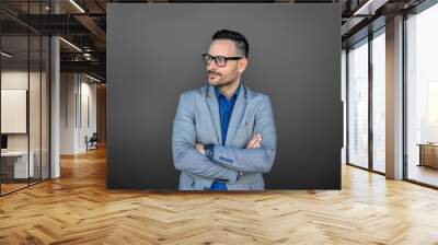 Confident young businessman with arms crossed looking away and thinking ideas on gray background Wall mural