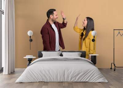 Ecstatic man and woman screaming and giving high five to each other while celebrating success. Excited young couple clapping hands and greeting while standing over yellow background Wall mural