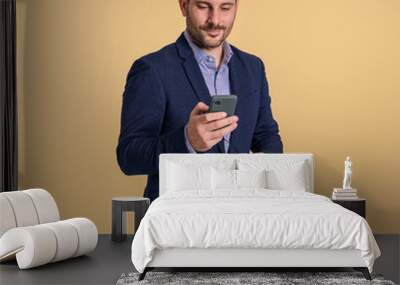 Elegant young businessman in suit checking social media over smart phone against beige background Wall mural