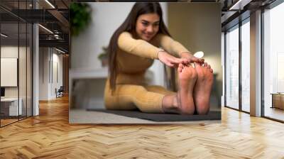 Fit, active and attractive young girl woman stretching before or after exercise at home maintaining healthy and fit way of living and daily physical activity lifestyle. Wall mural