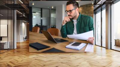 Focused young businessman auditing revenue report and planning budget while working at desk in office Wall mural