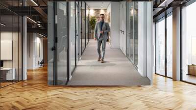 Full length of male professional in eyeglasses looking at camera while standing in office corridor Wall mural