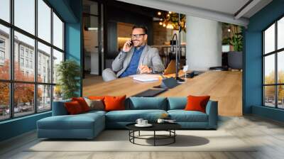 Handsome entrepreneur discussing over mobile phone while working on project at desk in modern office Wall mural