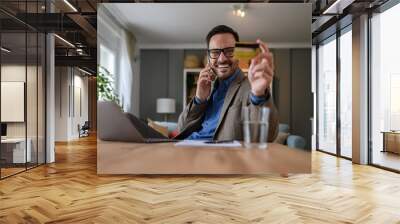 Handsome entrepreneur in elegant suit holding credit card and talking over smart phone at desk Wall mural