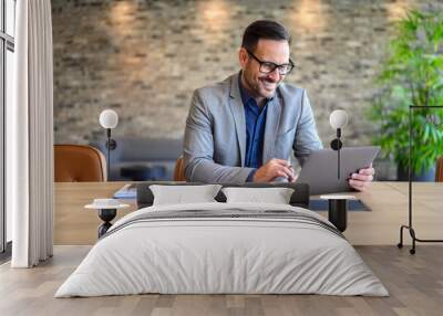 Handsome IT engineer in eyeglasses smiling and developing website over laptop on desk in modern office Wall mural