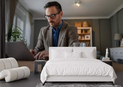 Low angle view of focused manager dressed in elegant suit working over laptop on desk at home Wall mural