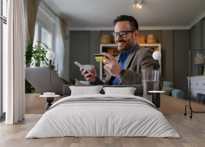 Low angle view of male professional paying with credit card over smart phone while sitting at desk Wall mural