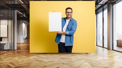 Mid adult cheerful businessman holding blank white banner template mock up and smiling at the camera while standing isolated against yellow background Wall mural