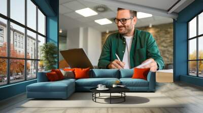 Portrait of financial analyst examining report and working on new strategies over laptop in office Wall mural