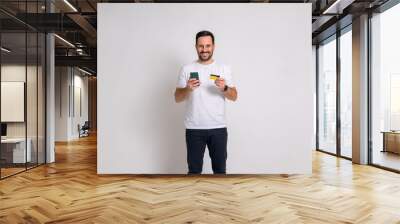 Portrait of happy male customer with credit card and smart phone standing over white background Wall mural