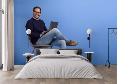 Portrait of male professional smiling and using wireless computer on chair against blue background Wall mural