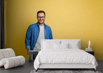 Portrait of smiling confident male entrepreneur with hands in pockets posing on yellow background Wall mural