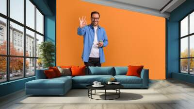 Portrait of smiling male professional using mobile phone and showing OK sign over orange background Wall mural