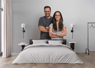 Portrait of smiling young couple wearing eyeglasses and casuals standing confidently against background. Joyful handsome man and beautiful woman posing with arms crossed Wall mural