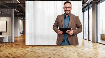 Portrait of young adult smiling cheerful man businessman entrepreneur standing against gray background backdrop hand held tablet and looking at camera. Wall mural