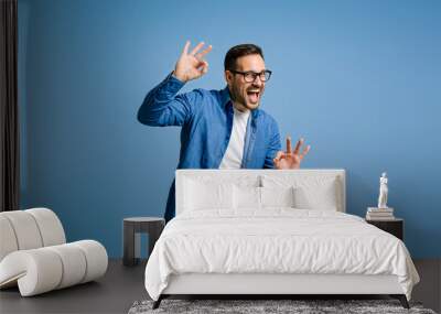 Satisfied businessman gesturing OK sign and shouting while standing against blue background Wall mural