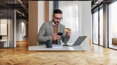 Serious businessman making credit card payment through smart phone at workplace Wall mural